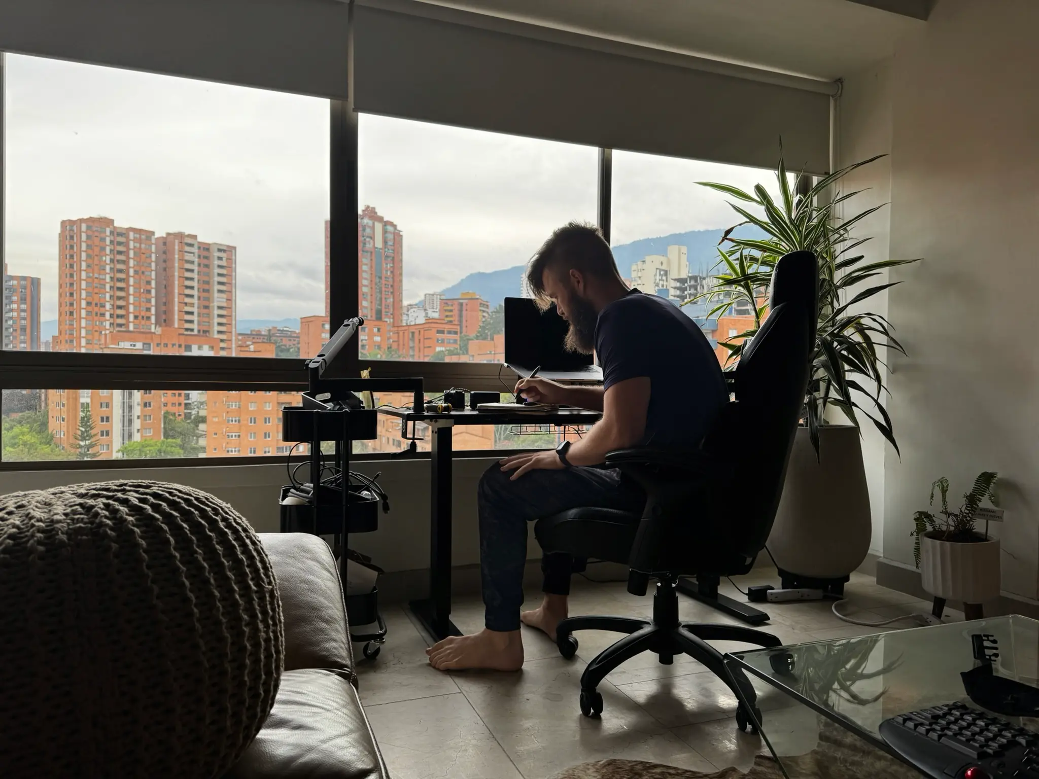 Ryan working at a desk by a window overlooking Medellín's brick high-rises